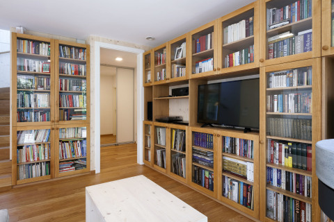 Povrchy v interiéru tvoří kombinace masivního dubu (podlahy), které jej ladí do zlatavých teplých odstínů, pohledově přiznaných CLT panelů s bílou lazurou a bílého sádrokartonu. Dominantou společné obývací části je mohutná na zakázku vyrobená knihovna