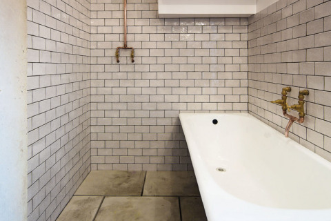 Koupelna s mosaznými armaturami, měděnými trubkami, plechovou vanou, betonovou dlažbou a glazovaným obkladem podobným jako v londýnském metru získala autentický industriální ráz