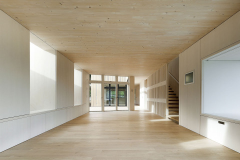 Dřevo vládne interiéru i exteriéru domu. Podlahy a stropy jsou z masivního materiálu, stěny jsou obloženy dýhovanými deskami. Výklenky ve stěně vlevo vedou ke střešním oknům, vpravo vytvořil architekt sedací kout integrovaný ve stěně