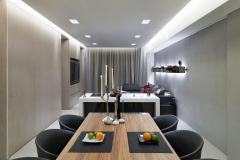 Čisté přehledné plochy minimalistického interiéru ožívají dynamickou hrou světel a stínů. Poklidný výraz spojitého obytného prostoru příjemně narušuje bohatě řasený závěs, rytmus židlí propsaný do stropních svítidel a zářící linie světel po stranách