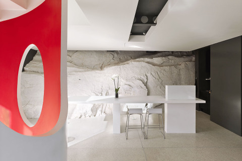 Společný obývací prostor přebírá bílé a šedé odstíny mramoru. Z hladké stěrky na podlaze „vyrůstá“ schodišťové těleso s oblými tvary, které designéři nazvali Dáma v červených šatech